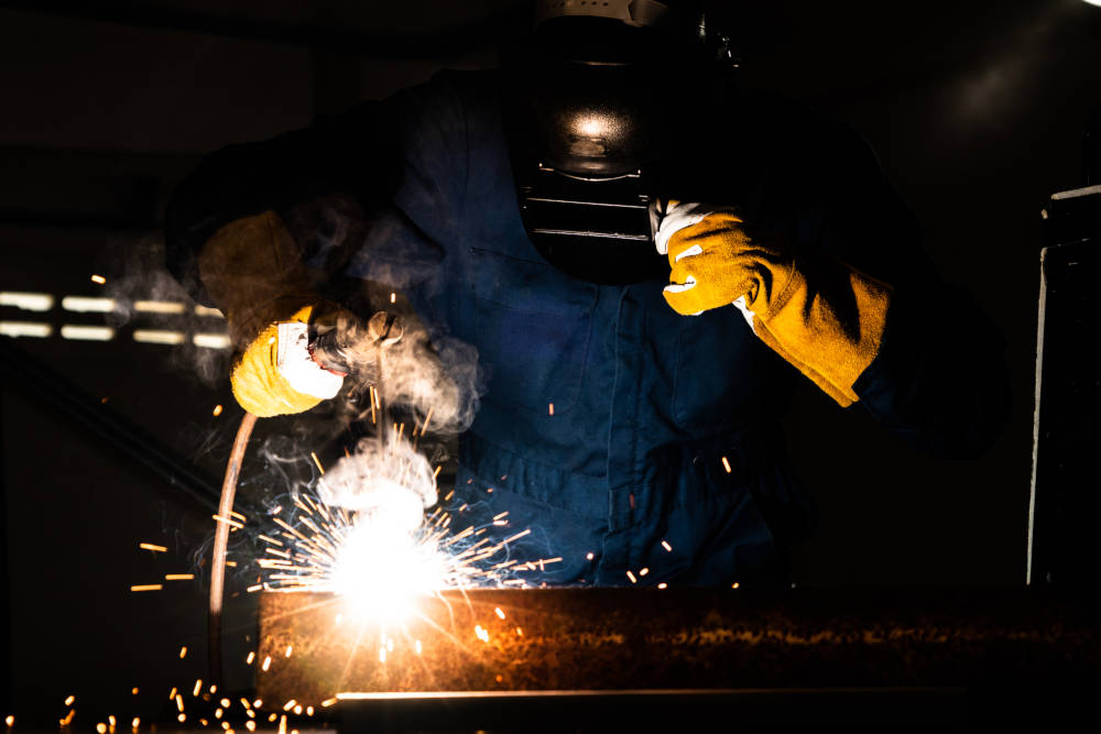 Metal welder working with arc welding machine to weld steel at factory while wearing safety equipment. Metalwork manufacturing and construction maintenance service by manual skill labor concept.